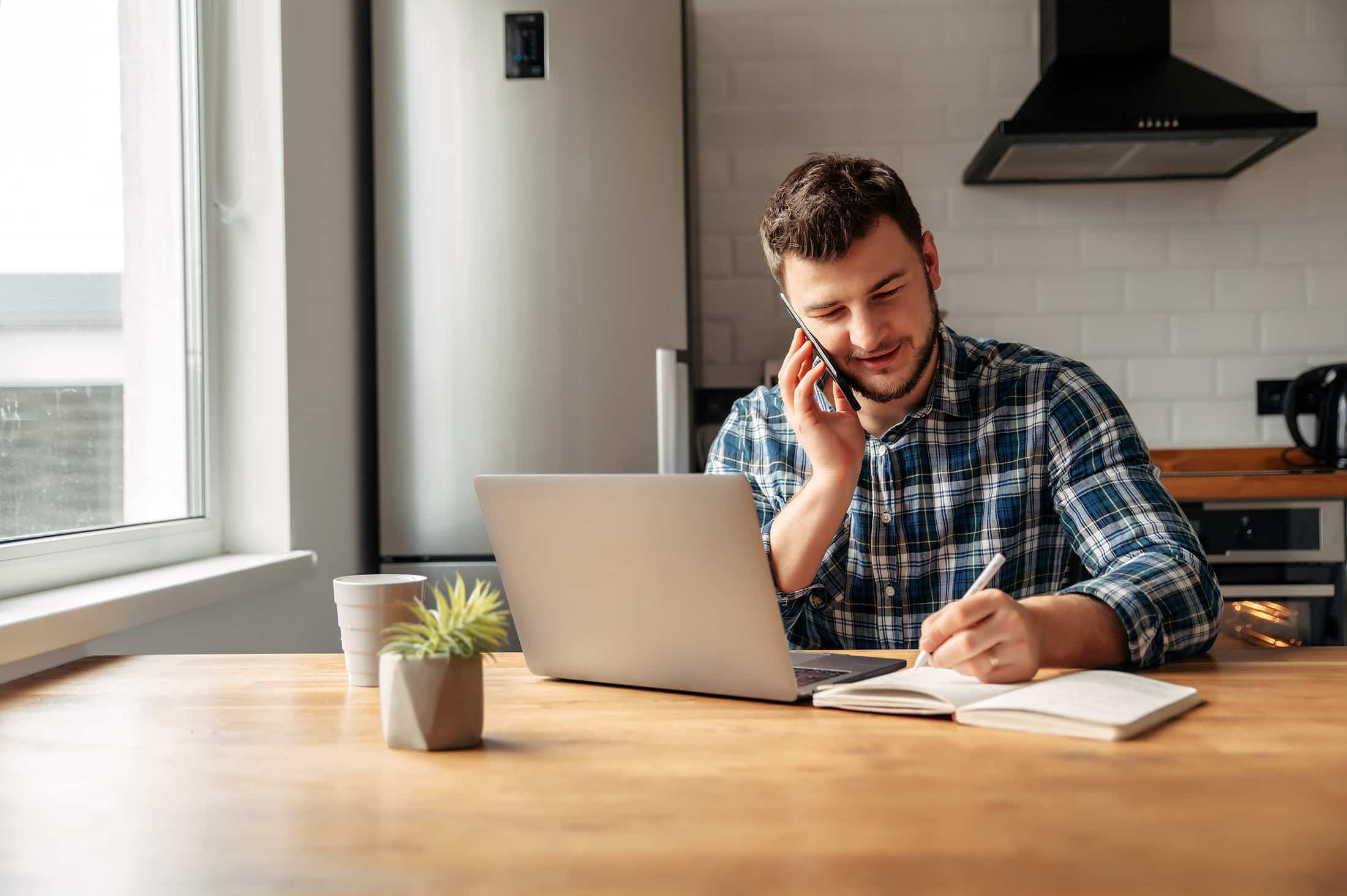 Man booking an HVAC appointment with ServicePlus in his kitchen with phone and laptop