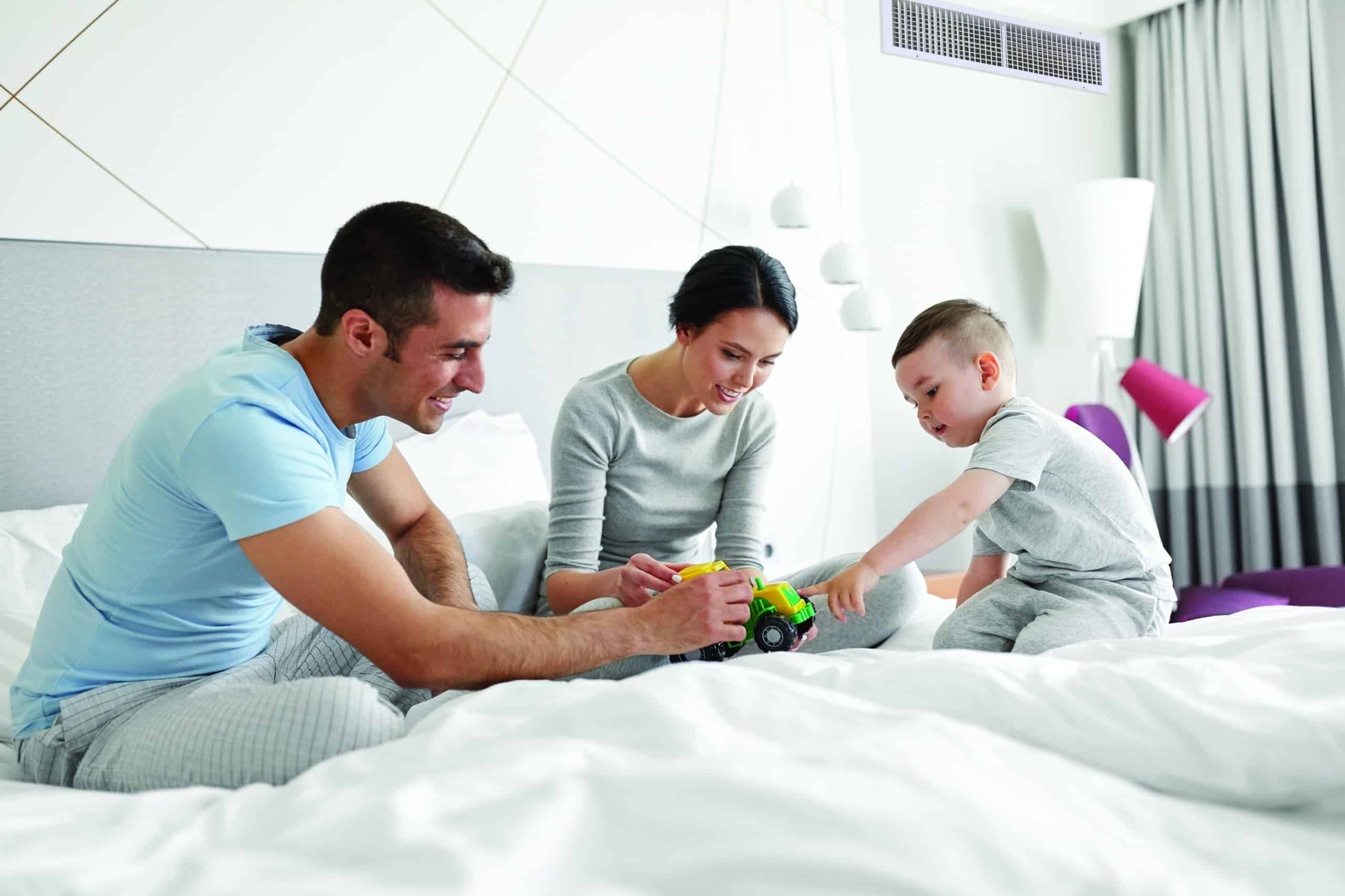 Photo of family playing with toys on the bed in the room with the inside unit of Skyair system visable.